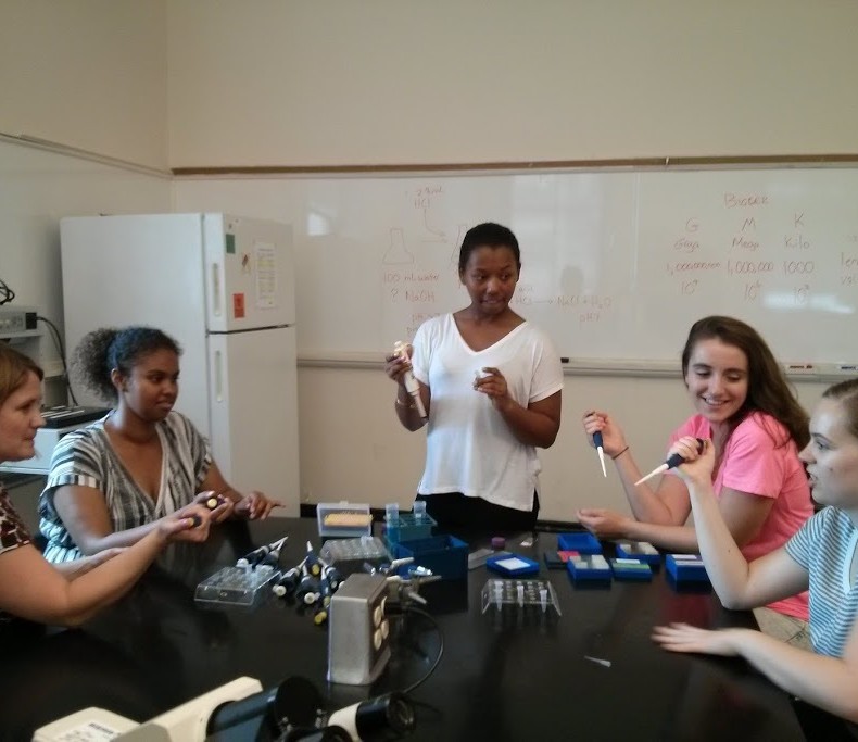 A professor, three students, and an Undergraduate Teaching Assistant practice using pipettes.